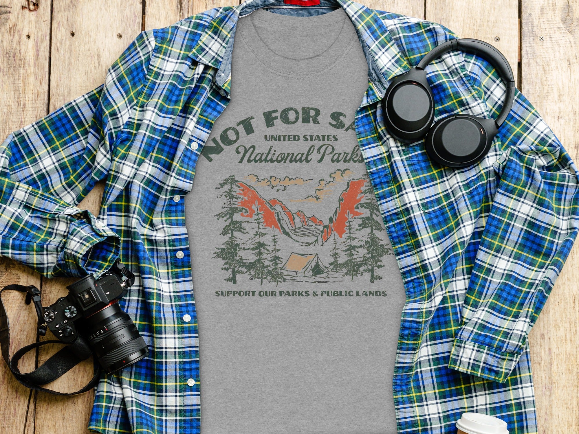 Grey t-shirt with "National Parks" graphic and plaid shirt, headphones, and camera accessories.