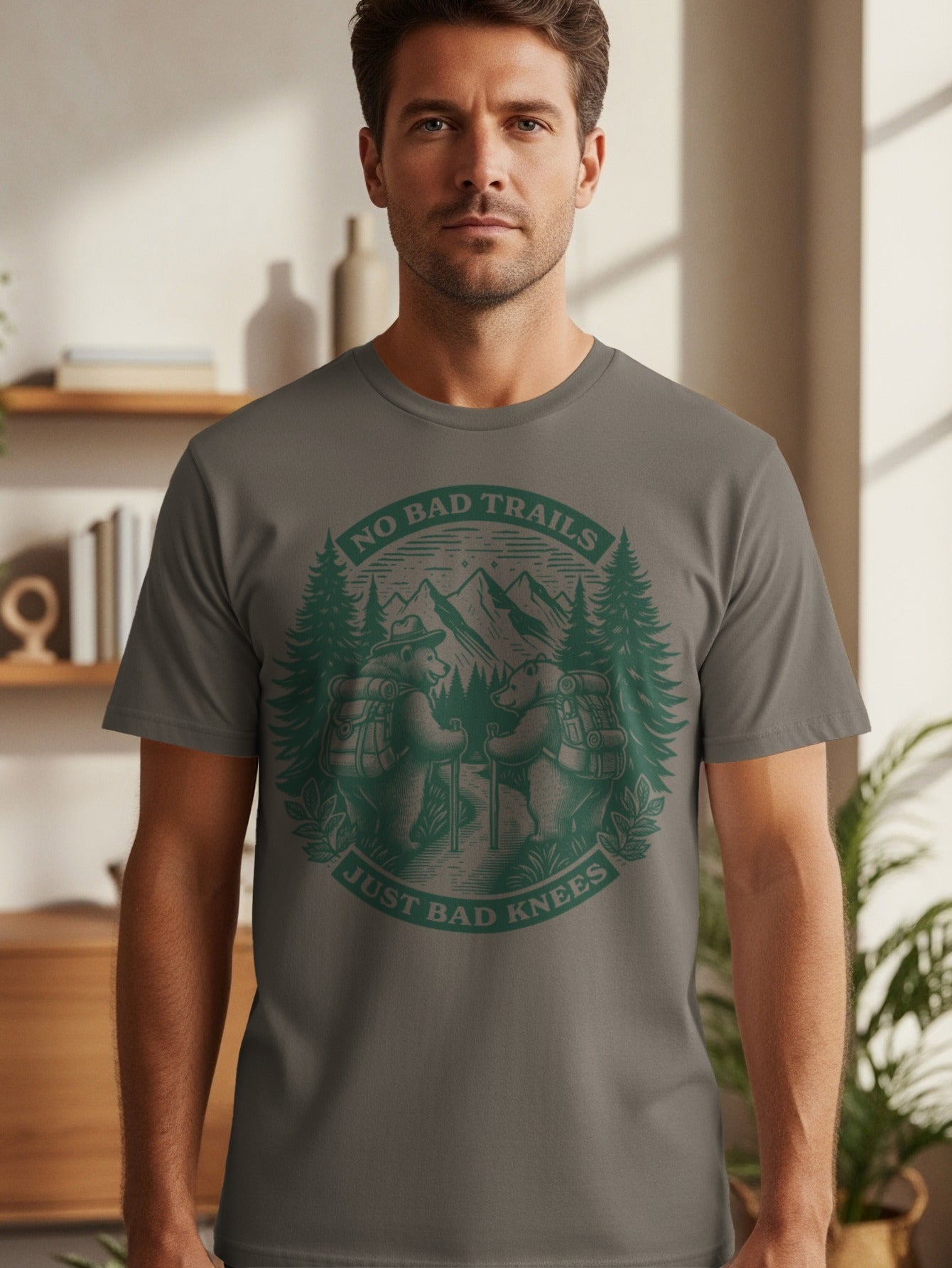 T-shirt with green graphic of two bears hiking, mountains, and trees. Text reads "NO BAD TRAILS JUST BAD KNEES".