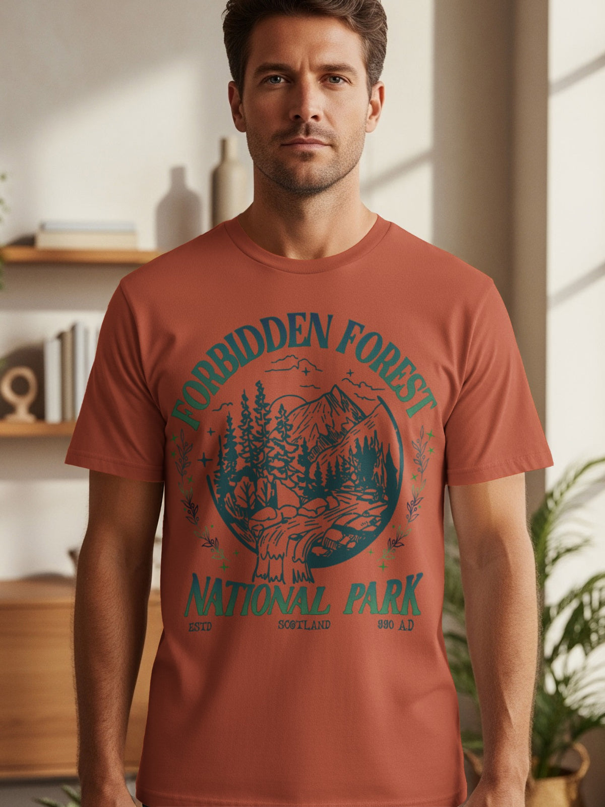 Terracotta t-shirt with circular graphic of mountains, trees, and waterfall, reading "Forbidden Forest National Park Scotland".