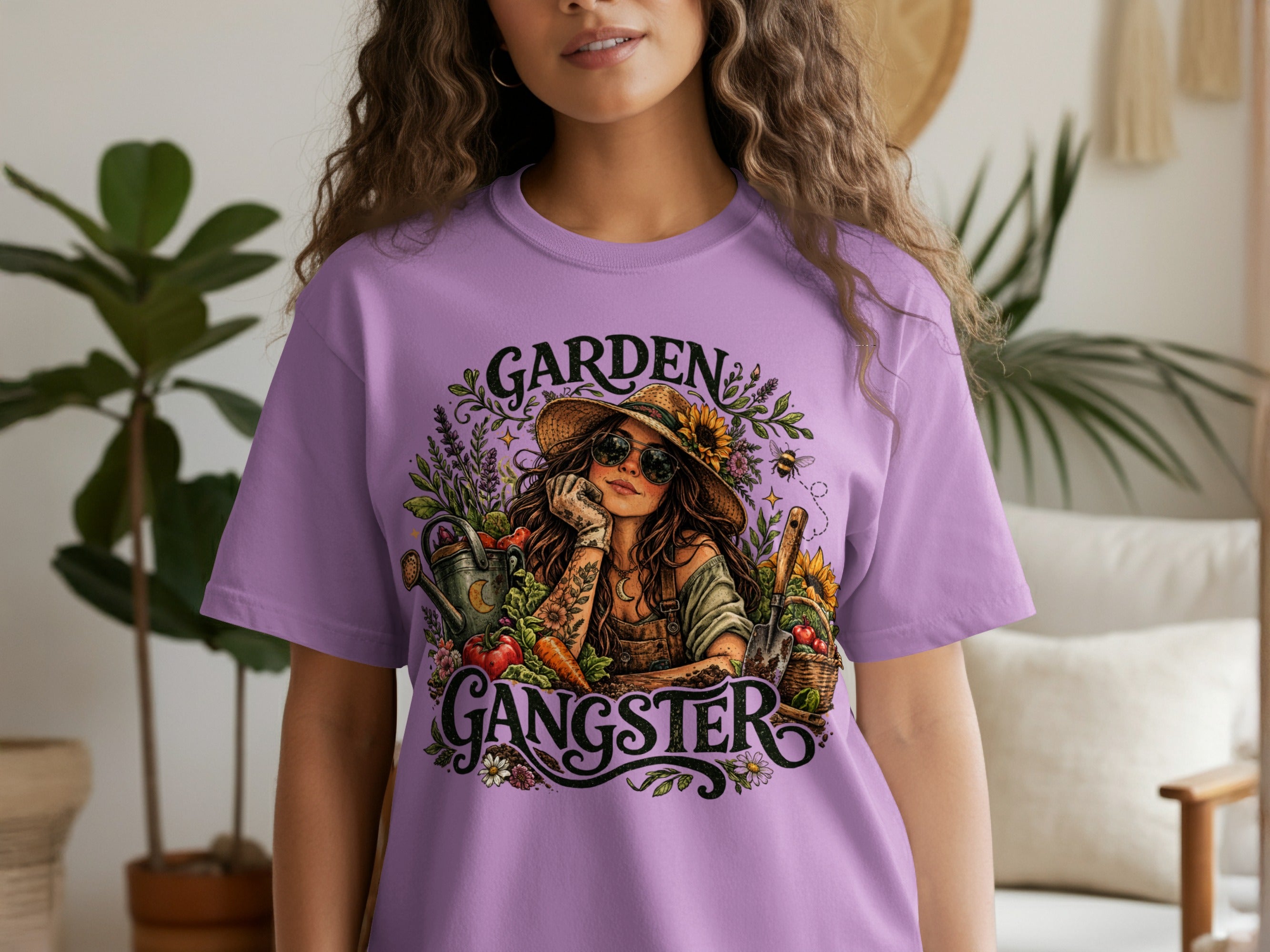 Lilac t-shirt with "Garden Gangster" graphic of a woman in a straw hat surrounded by gardening elements.