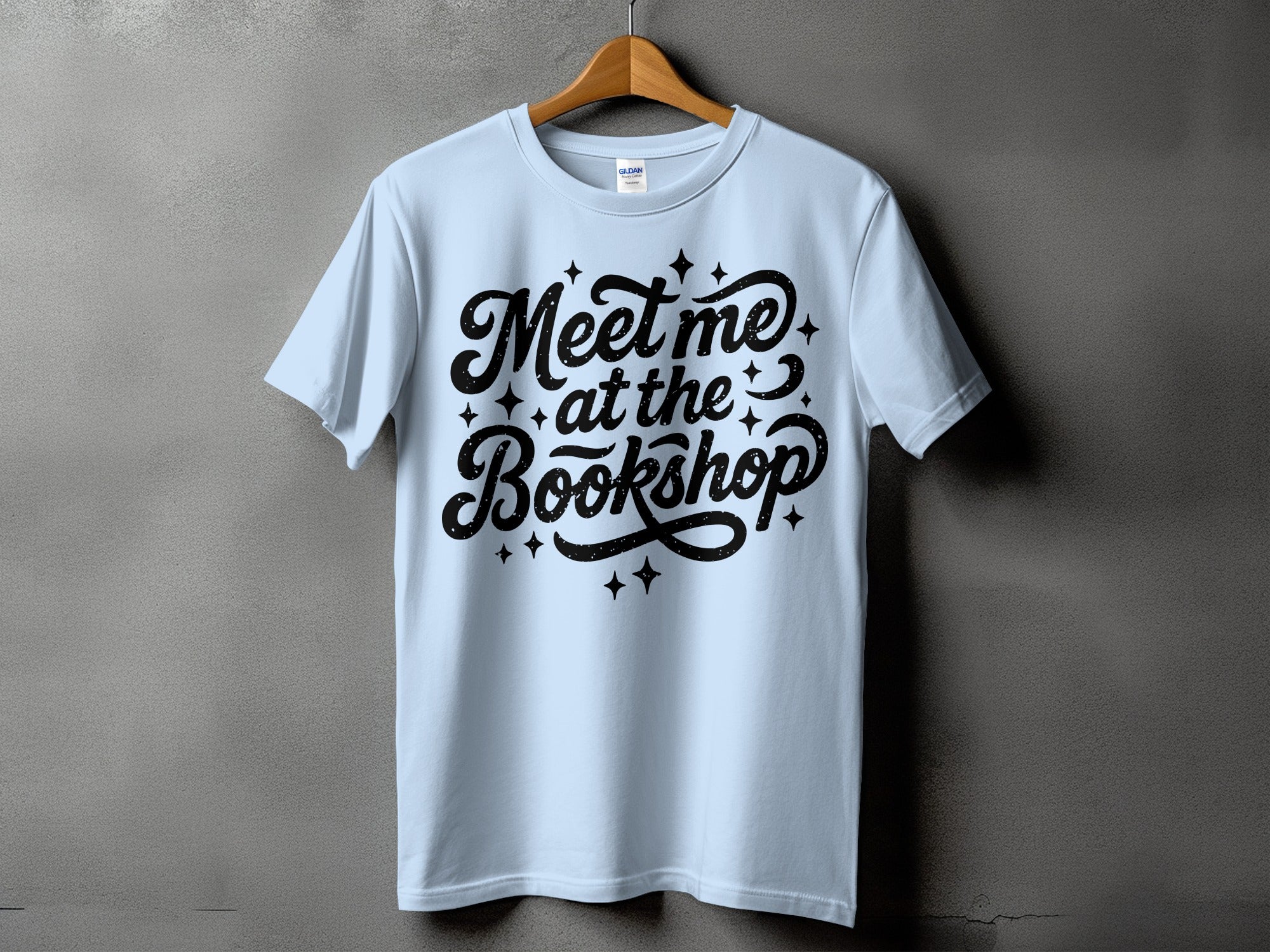 Light blue t-shirt with black text "Meet me at the Bookshop" and stars.