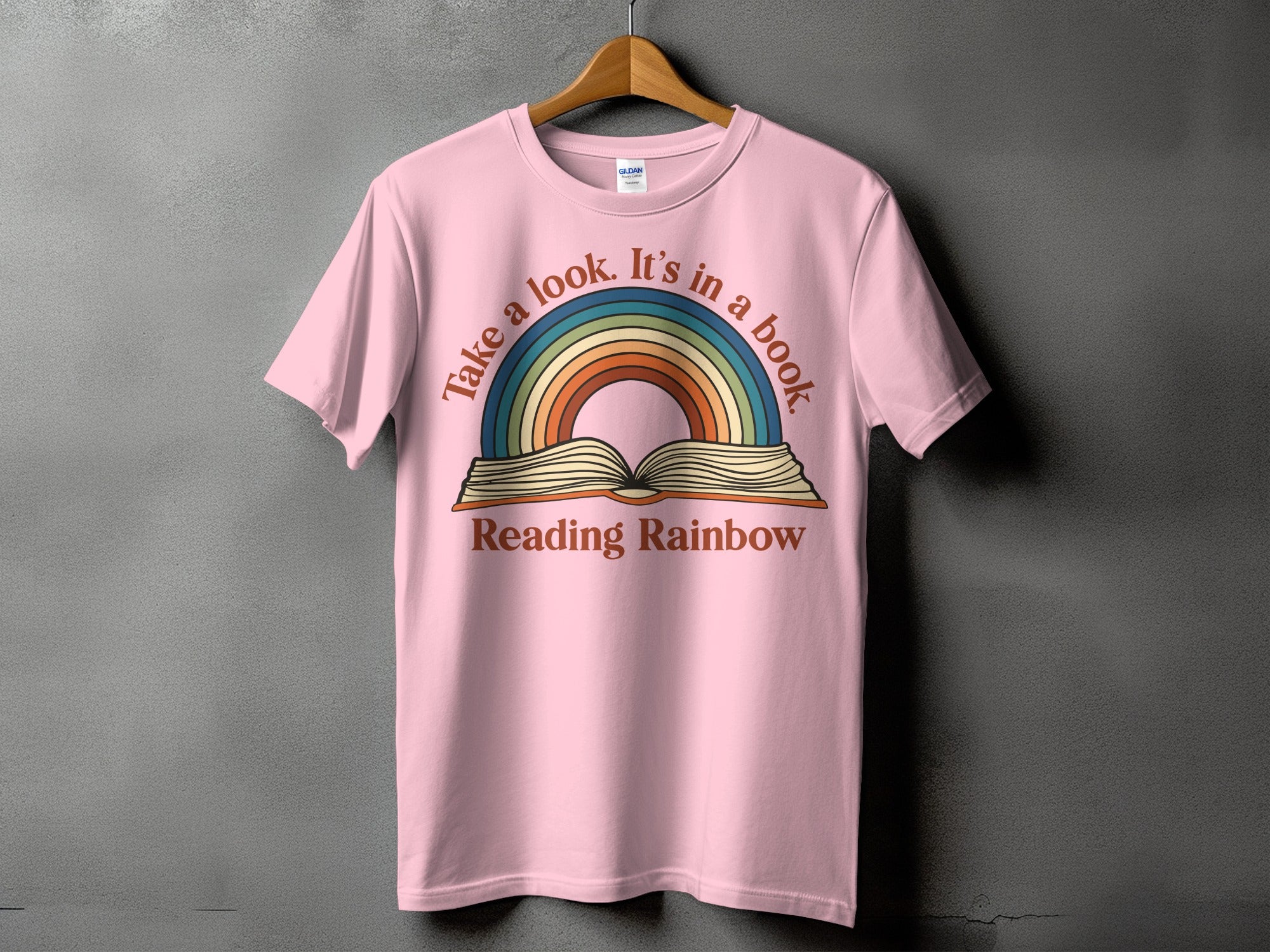 Pink t-shirt with rainbow and book graphic reading "Take a look. It's in a book. Reading Rainbow."