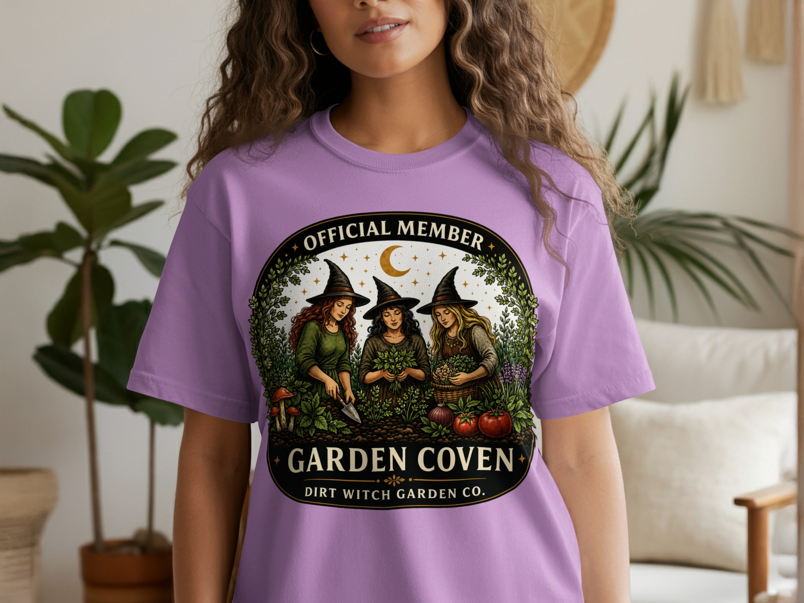 T-shirt graphic: Three witches gardening under a crescent moon with "Garden Coven" text.