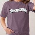 Purple t-shirt with a black and white banner graphic that reads "CALM YOUR TITS".