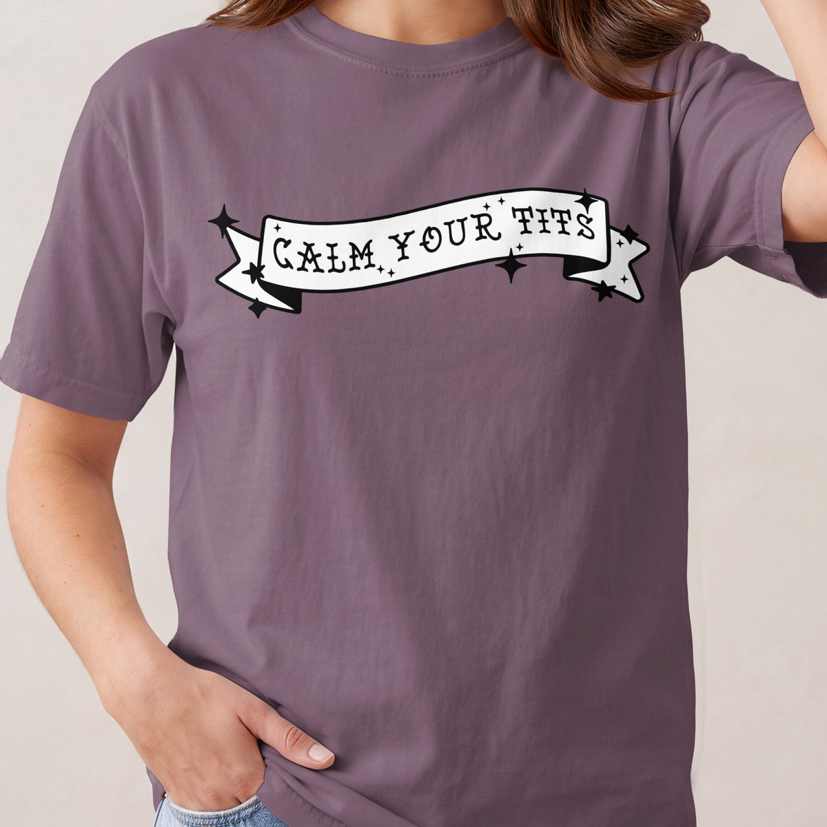 Purple t-shirt with a black and white banner graphic that reads "CALM YOUR TITS".