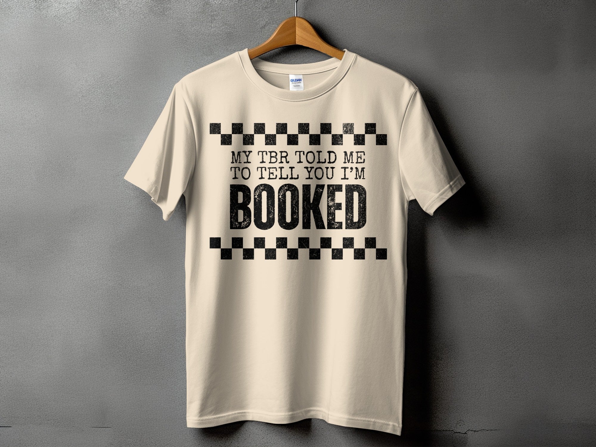 Light beige t-shirt with black text "MY TBR TOLD ME TO TELL YOU I'M BOOKED".