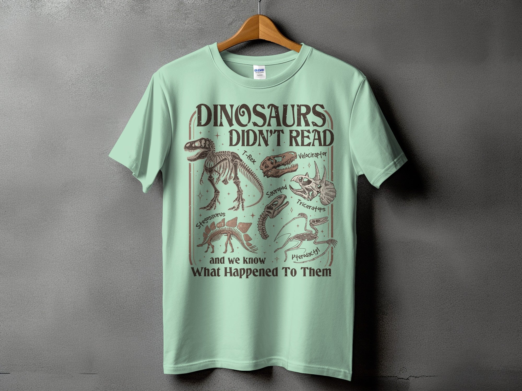 Mint t-shirt with graphic "Dinosaurs Didn't Read" and dinosaur skeletons.
