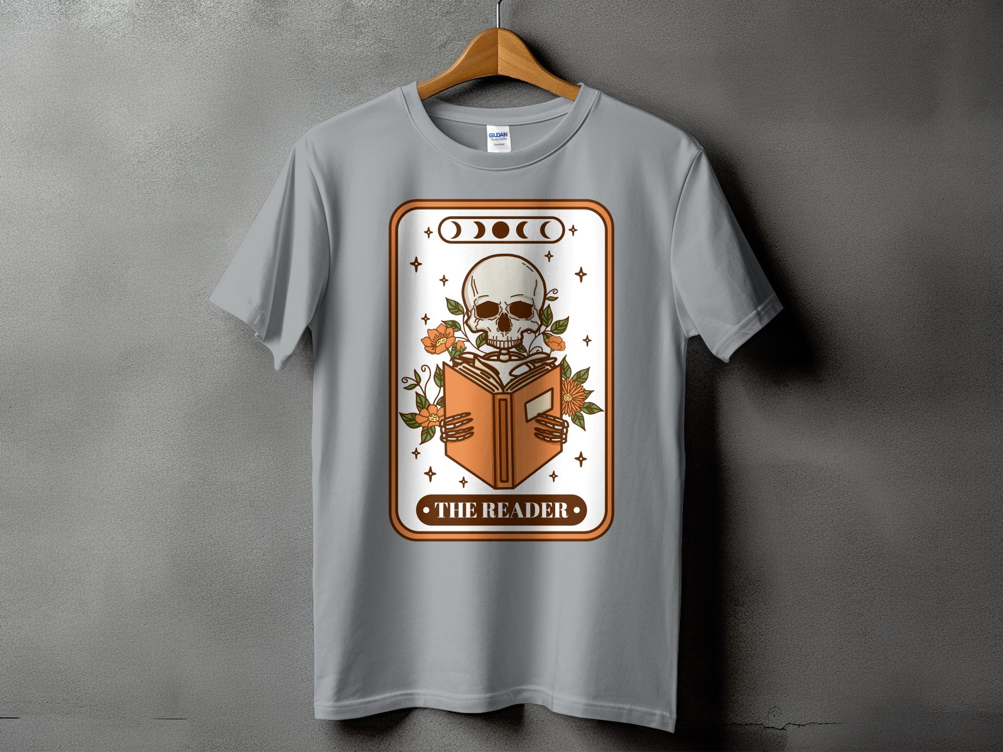 T-shirt graphic of skeleton reading an open book with flowers and moon phases.