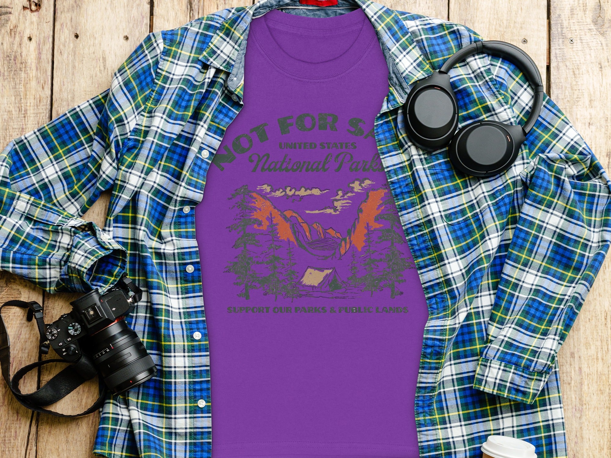 Purple t-shirt with National Park graphic and text, laid flat with flannel shirt and accessories.