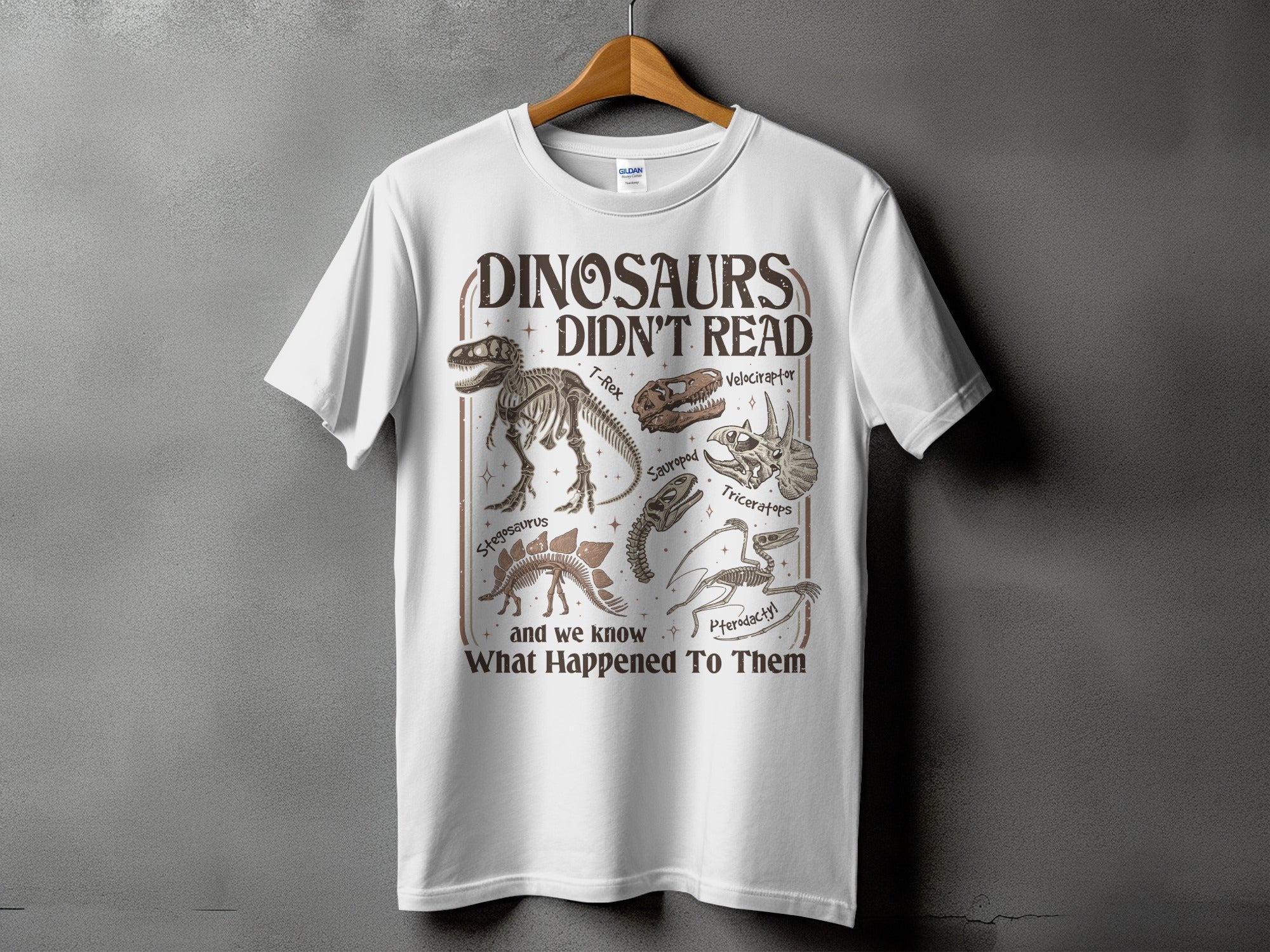 White t-shirt with "Dinosaurs Didn't Read" and dinosaur skeletons.