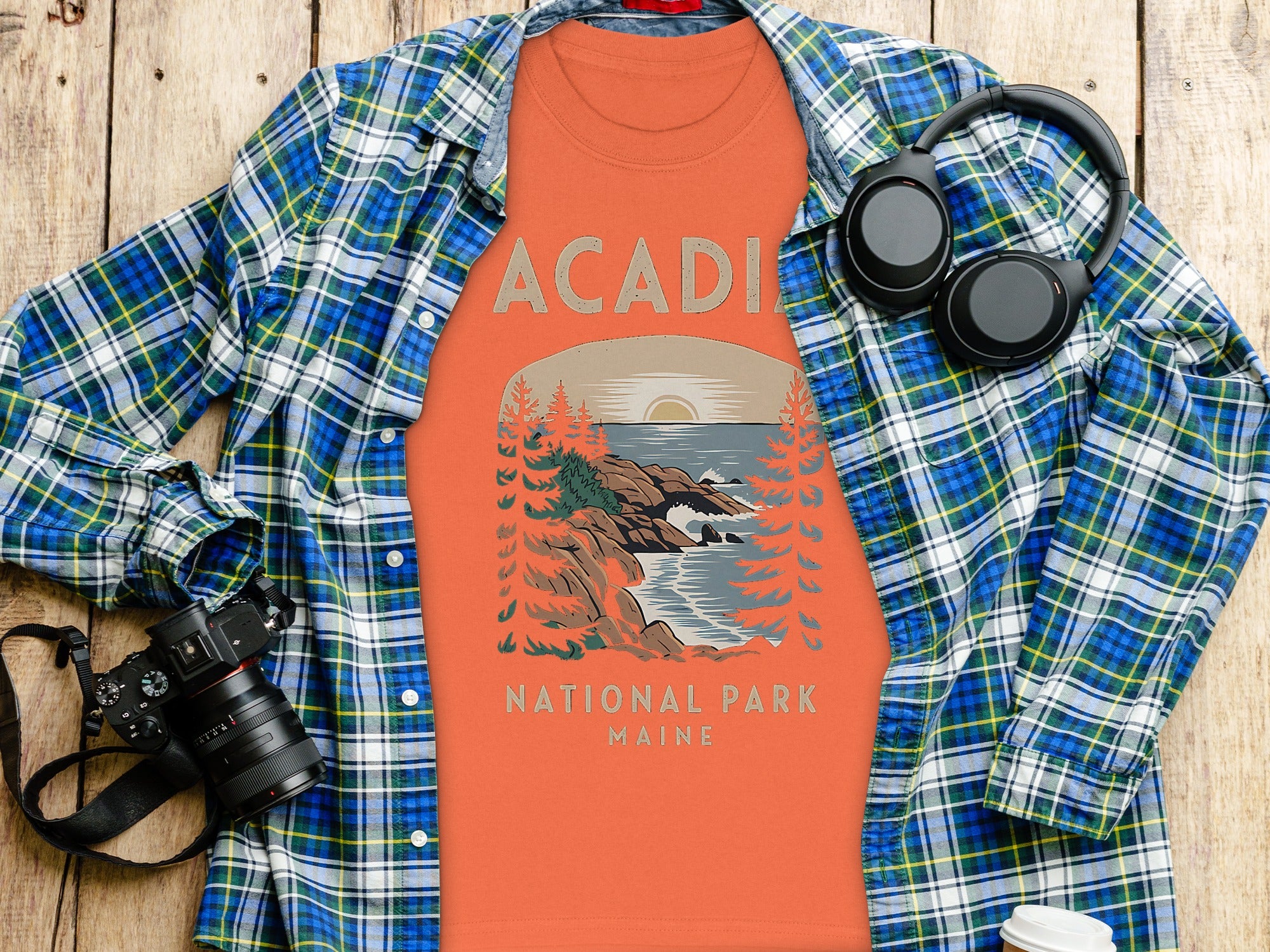 Orange t-shirt with Acadia National Park Maine graphic, plaid shirt, headphones, and camera.