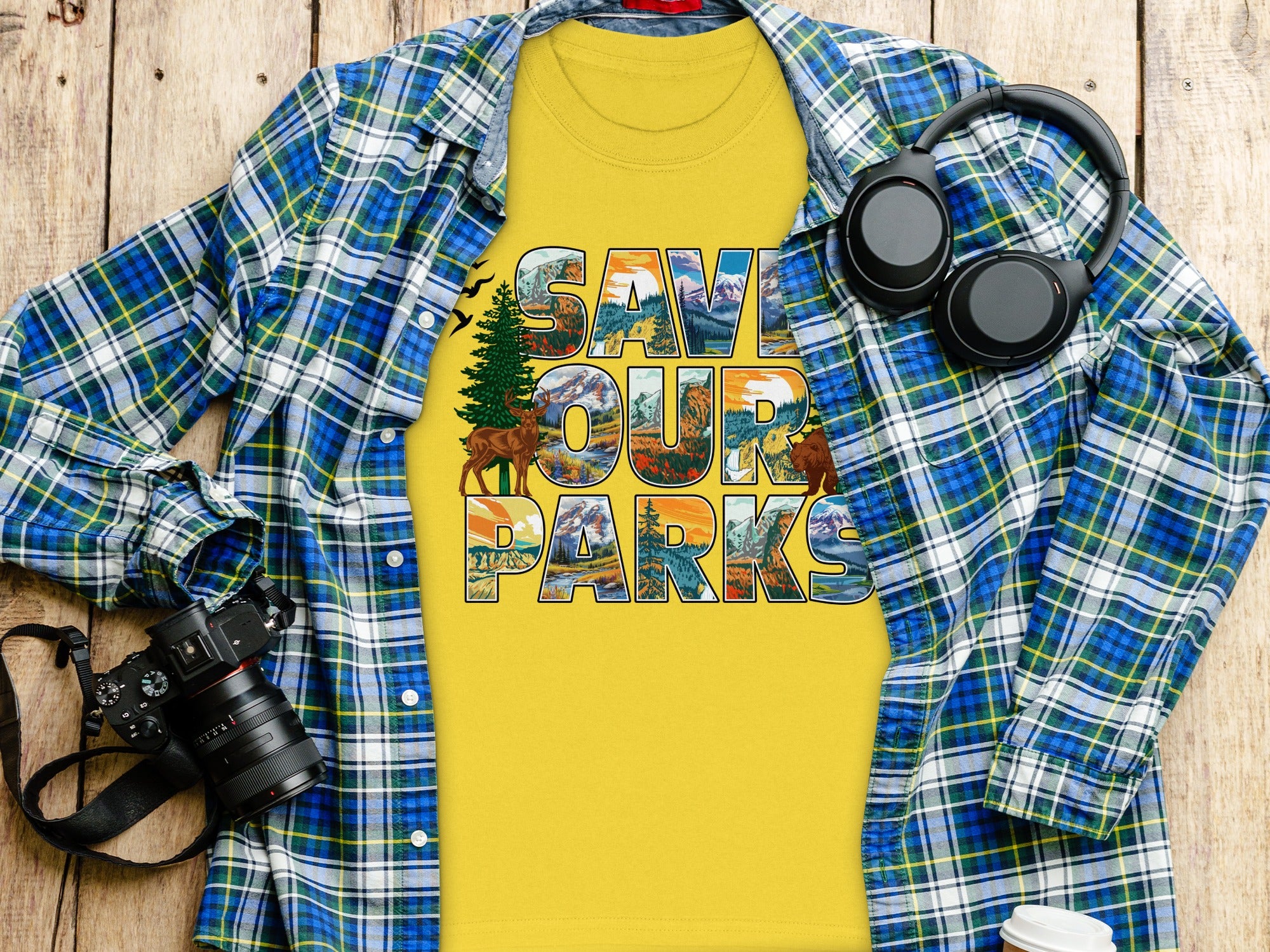 Yellow t-shirt with "SAVE OUR PARKS" text featuring outdoor scenic art, plaid shirt, camera, and headphones.