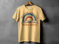 Yellow t-shirt with a graphic featuring an open book and rainbow, text reads "Take a look. It's in a book."
