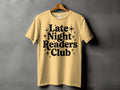 Yellow t-shirt with black text reading "Late Night Readers Club" and starburst accents.