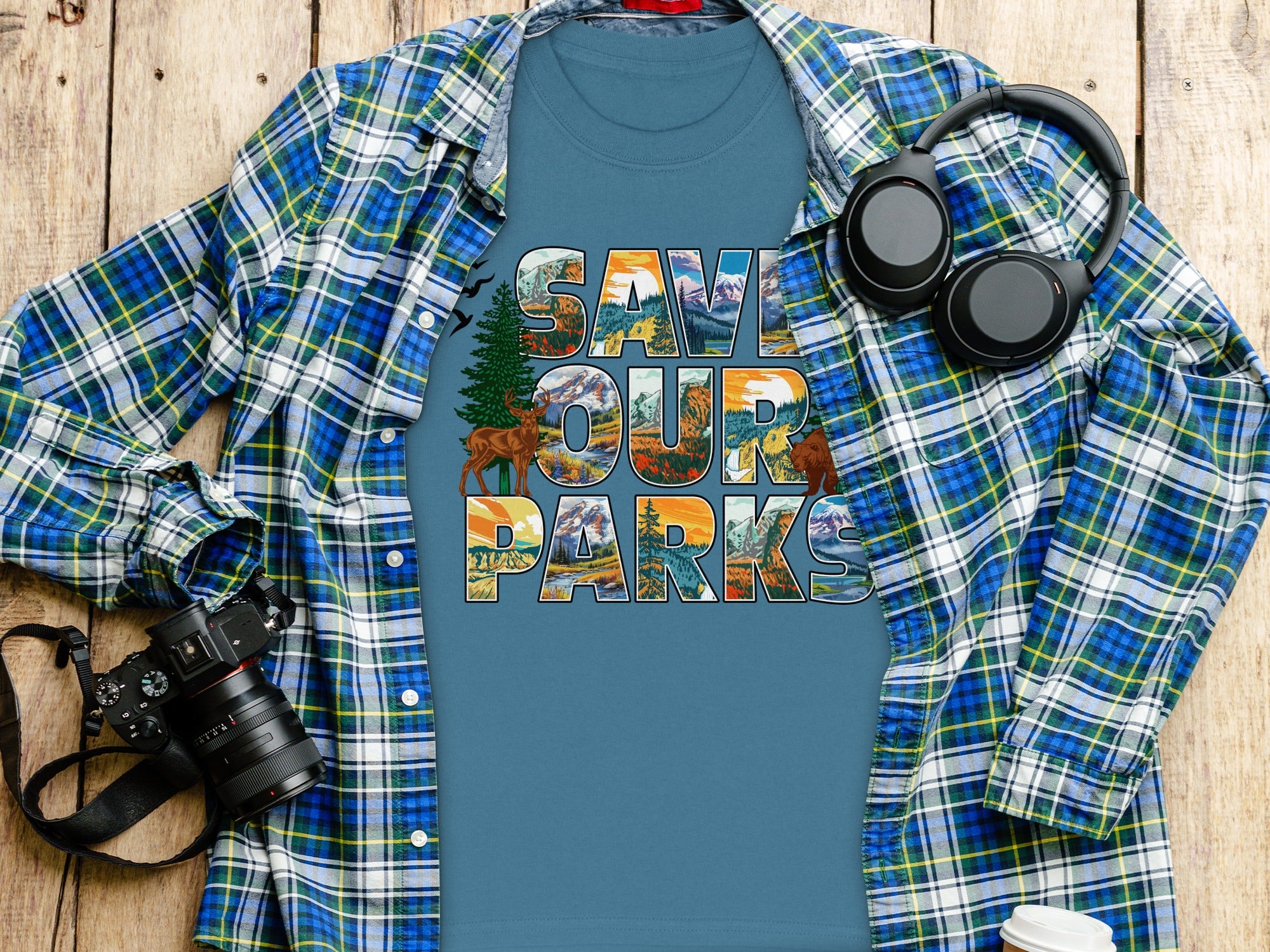 Blue t-shirt with "Save Our Parks" text and nature graphics, laid flat with plaid shirt.