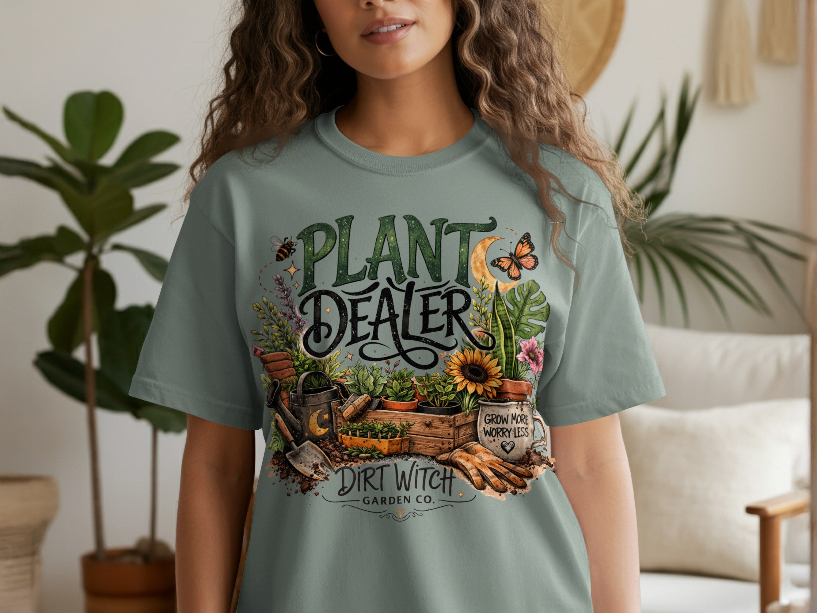 "Plant Dealer" graphic on a sage green t-shirt with gardening motifs and "Dirt Witch Garden Co." text.