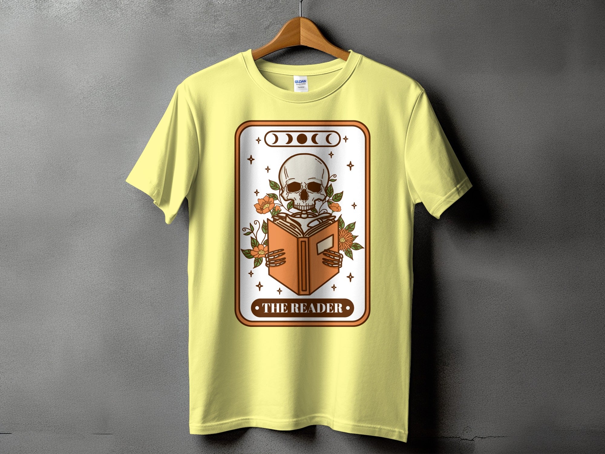 Pale yellow t-shirt with a graphic of a skeleton reading a book and the text "The Reader."