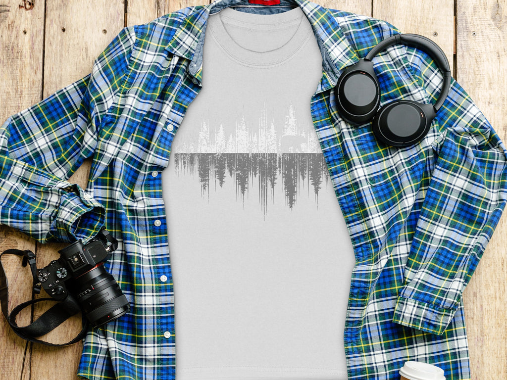 Grey t-shirt with forest and bear graphic, framed by plaid shirt, headphones, and camera.
