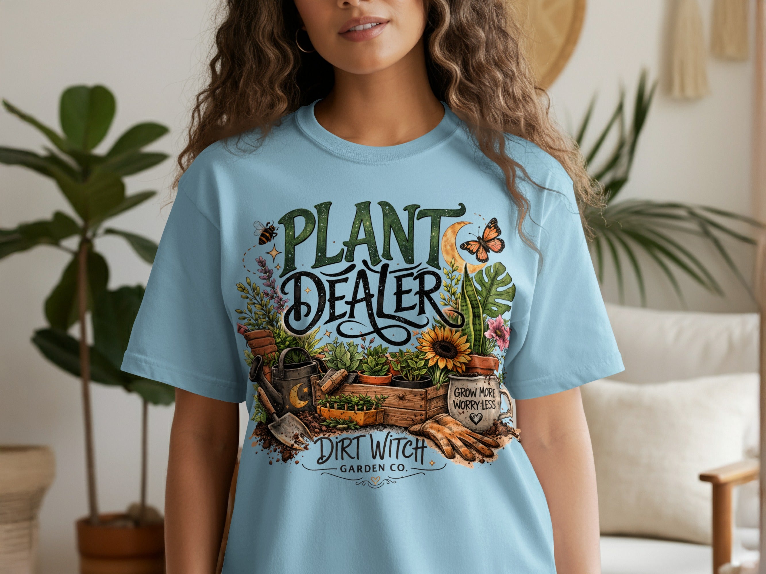 Light blue t-shirt with "Plant Dealer" design, gardening tools, and "Dirt Witch Garden Co."