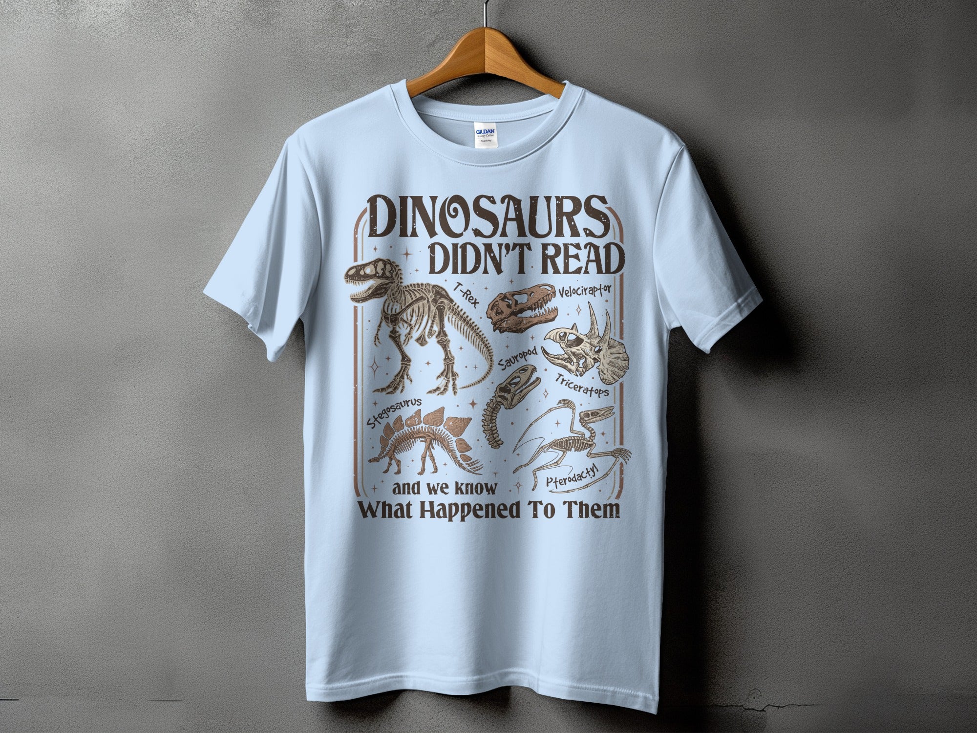 Light blue t-shirt with text "DINOSAURS DIDN'T READ" and dinosaur skeleton illustrations.