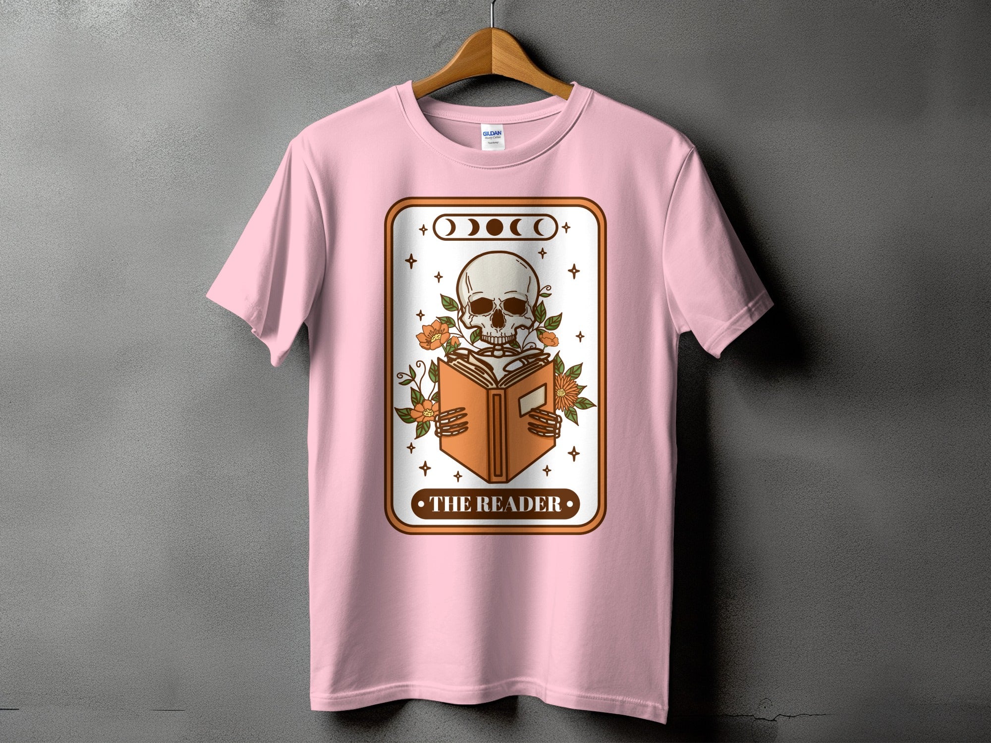 Pink t-shirt with a skeleton reading a book and "The Reader" text.