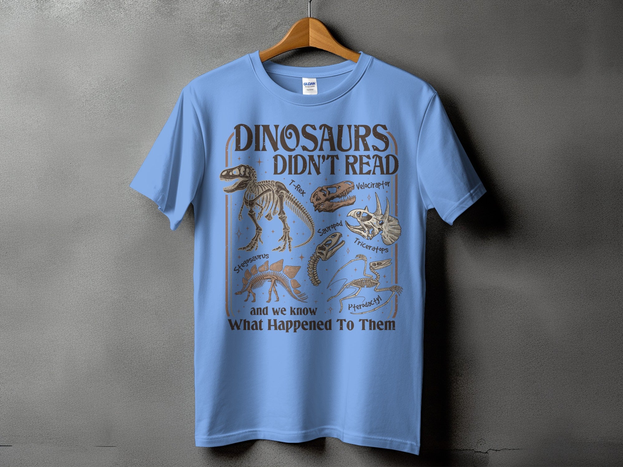 Light blue t-shirt with text "Dinosaurs Didn't Read" and dinosaur skeletons.