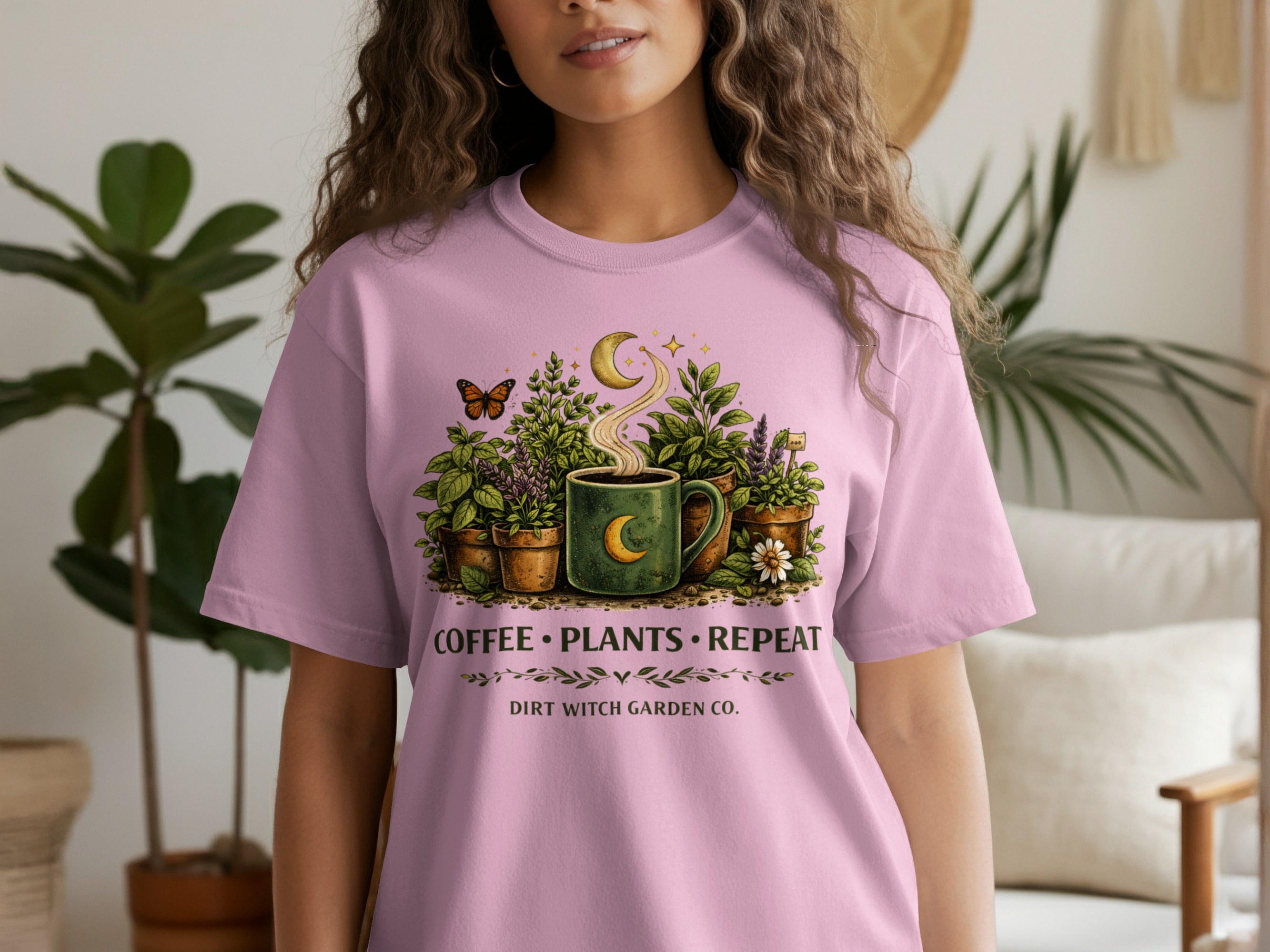 Pink t-shirt with graphic of coffee, plants, moon, stars, and butterfly. Text says "Coffee Plants Repeat" and "Dirt Witch Garden Co.".