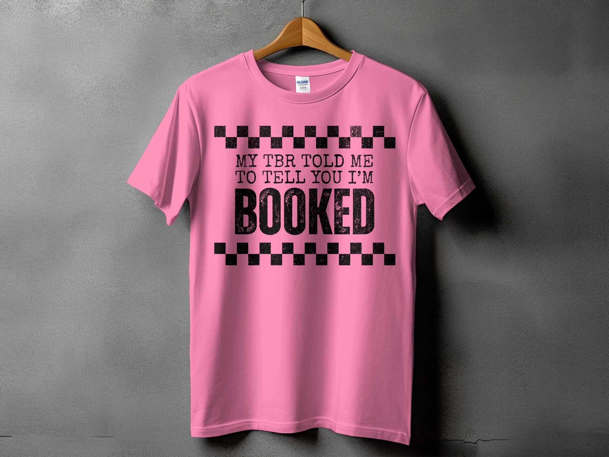 Pink t-shirt with black text saying "MY TBR TOLD ME TO TELL YOU I'M BOOKED".