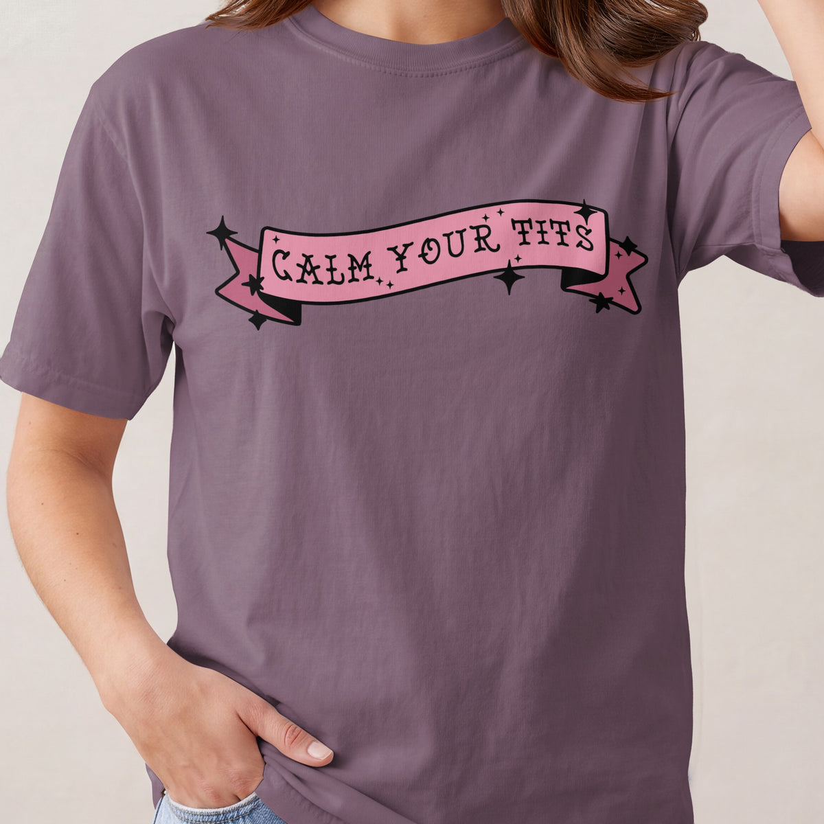 Purple t-shirt with pink banner graphic that reads "Calm Your Tits".