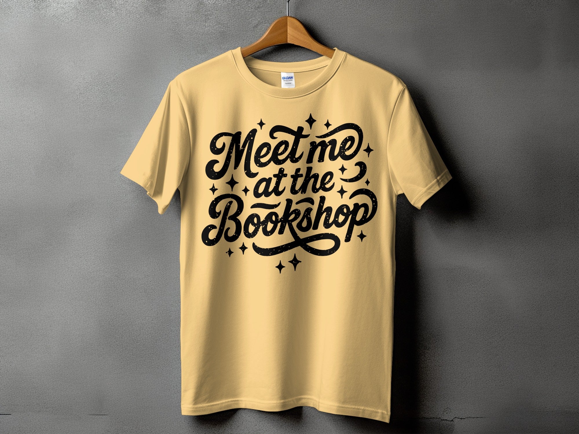 Yellow t-shirt with black text "Meet me at the Bookshop" and star accents.