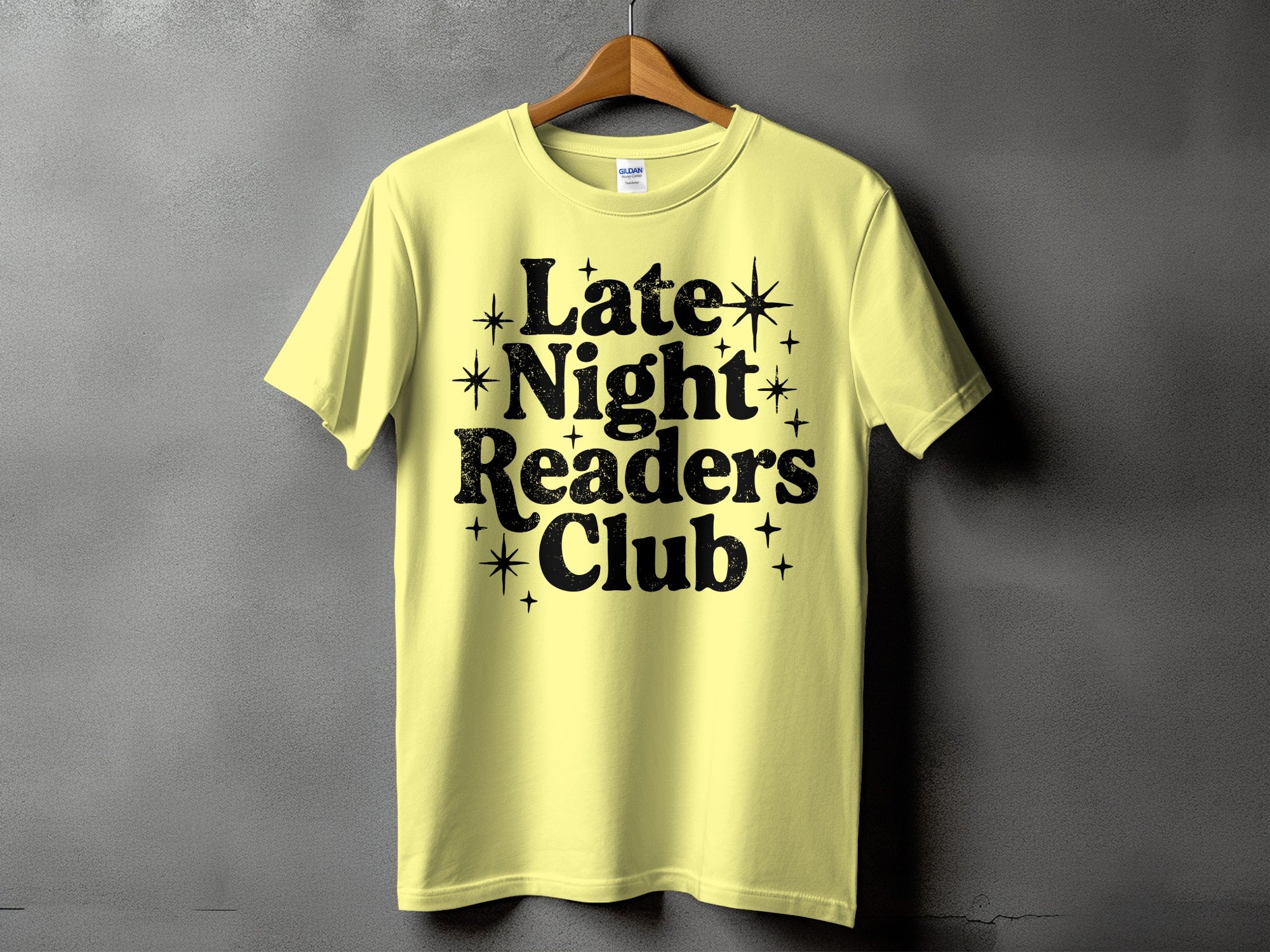 Yellow t-shirt with black text reading "Late Night Readers Club" and small star accents.