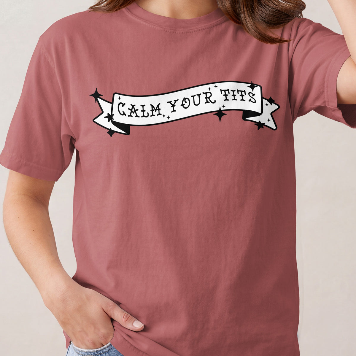 Rose t-shirt with a white banner graphic reading "CALM YOUR TITS."