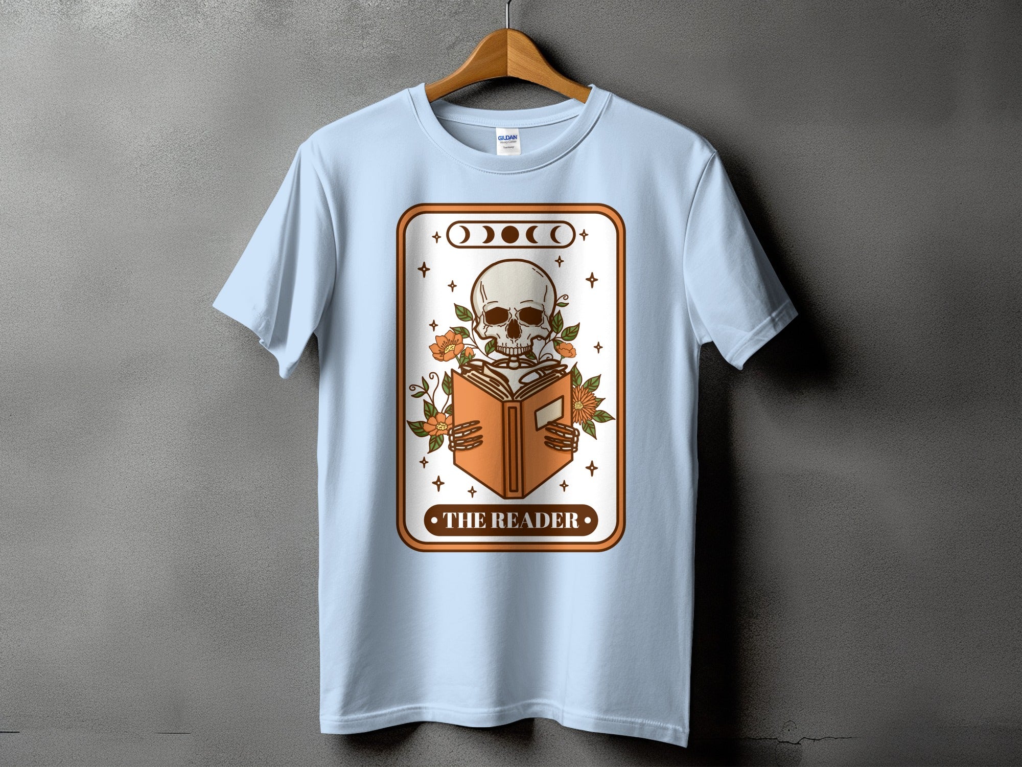 Light blue t-shirt with a graphic of a skeleton reading a book, titled "The Reader."